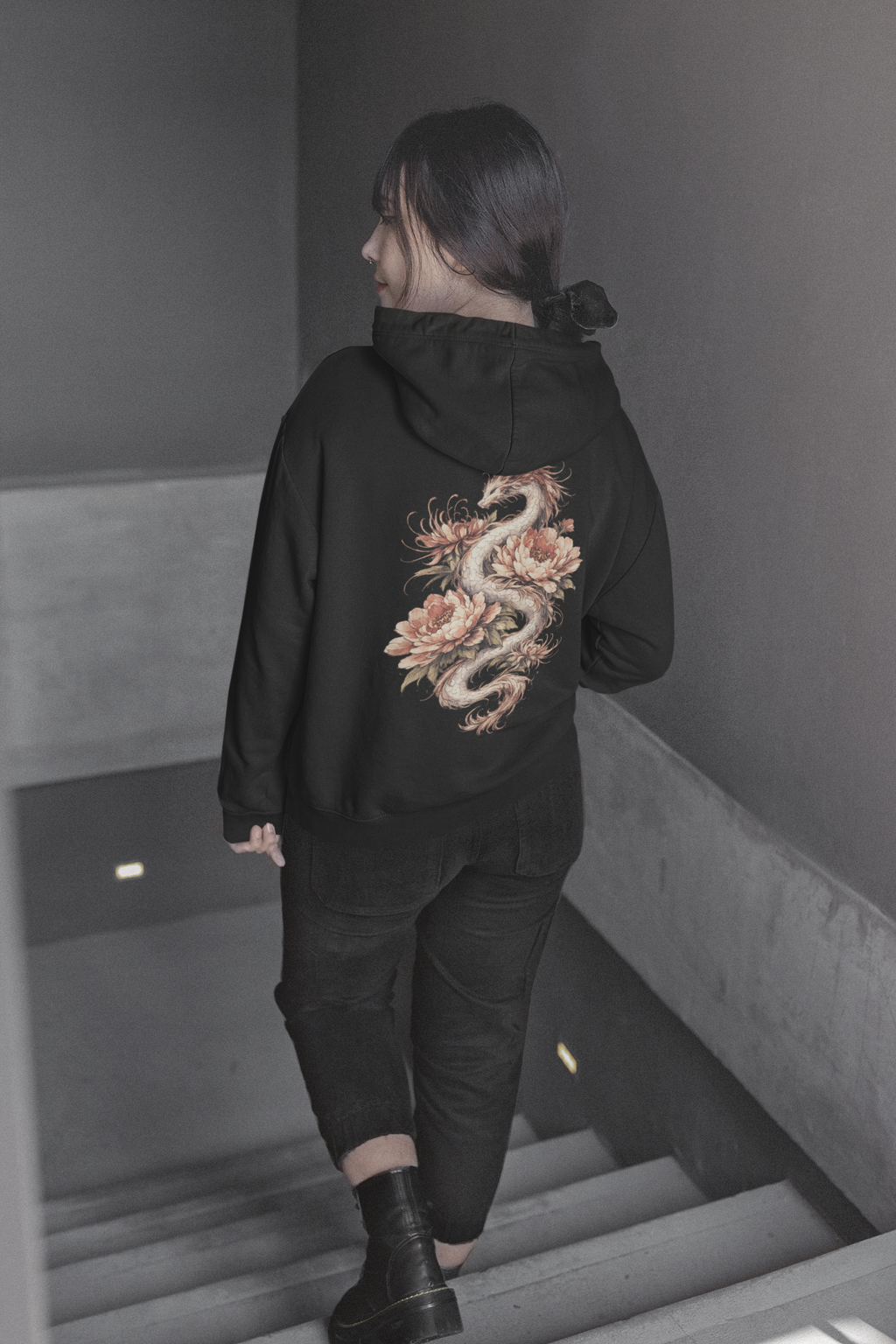 Person wearing a black hoodie with a dragon design on the back, walking down stairs.