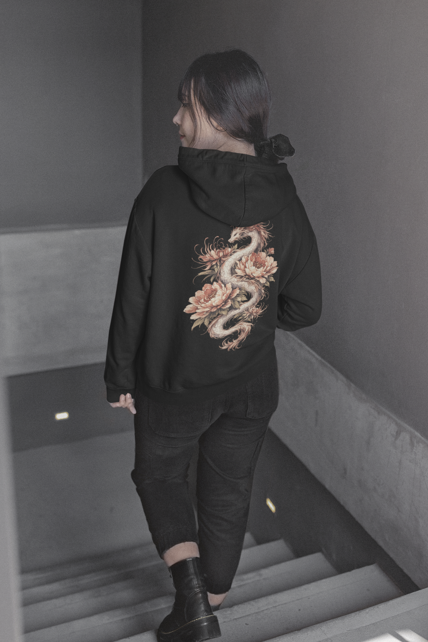 Person wearing a black hoodie with a dragon design on the back, walking down stairs.