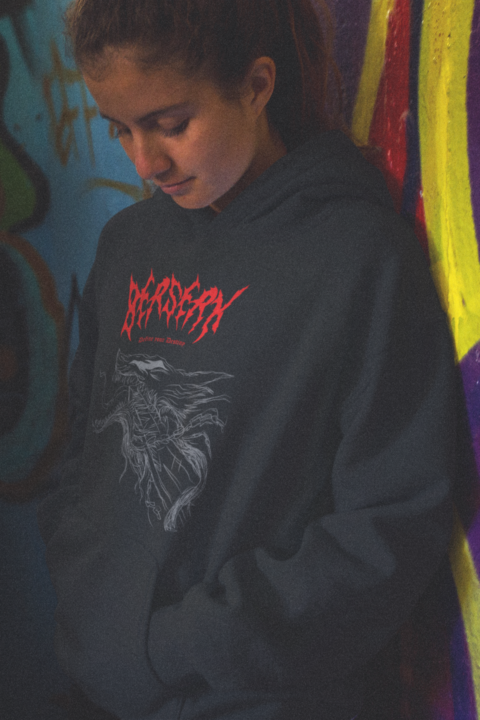 Person wearing a black hoodie with red text in front of a colorful graffiti wall.