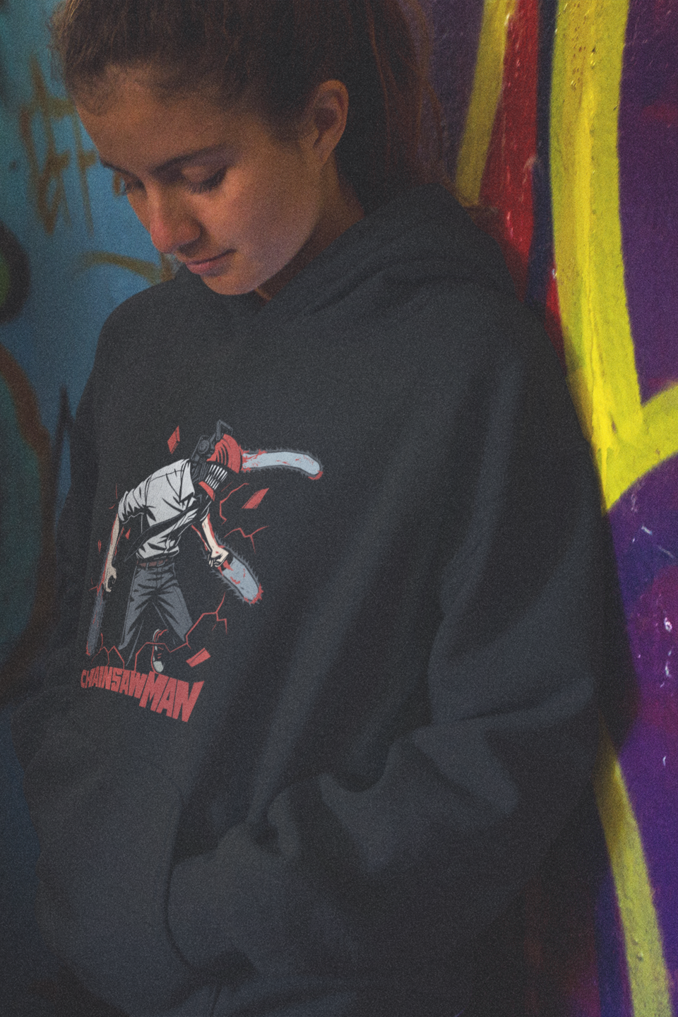 Person wearing a black hoodie with a graphic design in front of a colorful graffiti wall.